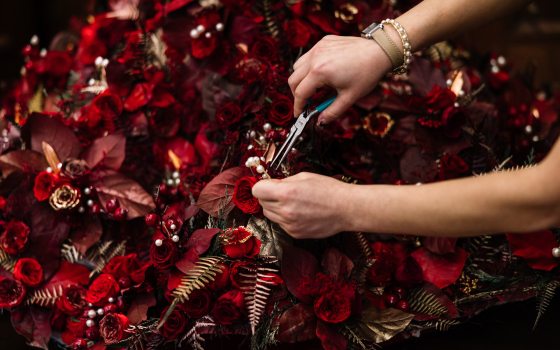 a person with pliers near a floral bouquet of red and gold flowers and leaves